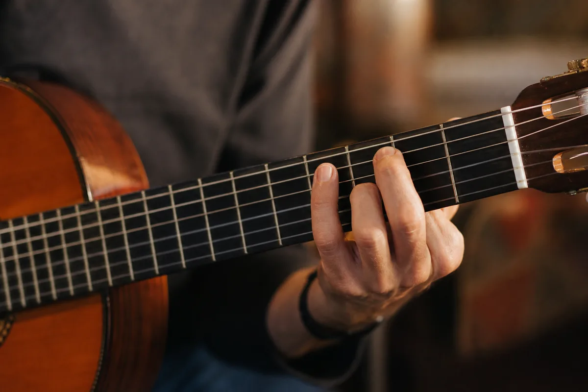 Mains d&rsquo;un musicien pressant une case sur le manche d&rsquo;une guitare à cordes nylon