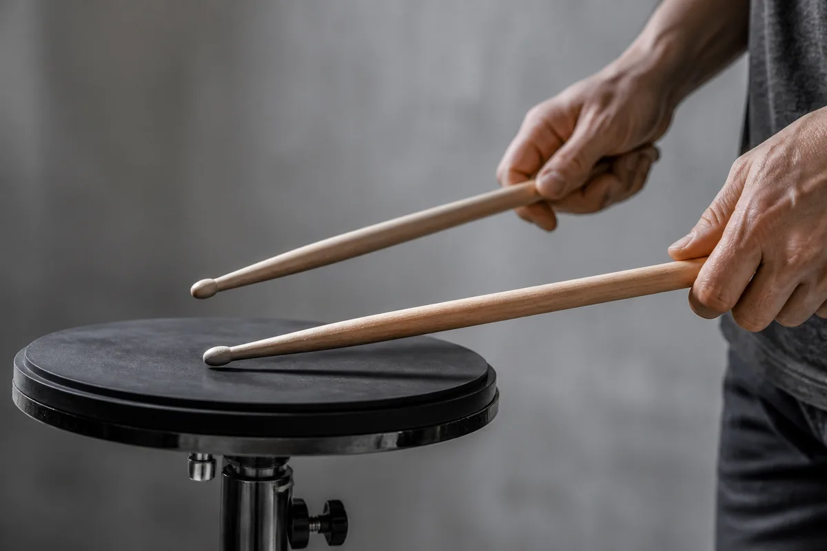 Mains d un batteur tenant deux baguettes au-dessus d un pad d entraînement posé sur un pied réglable