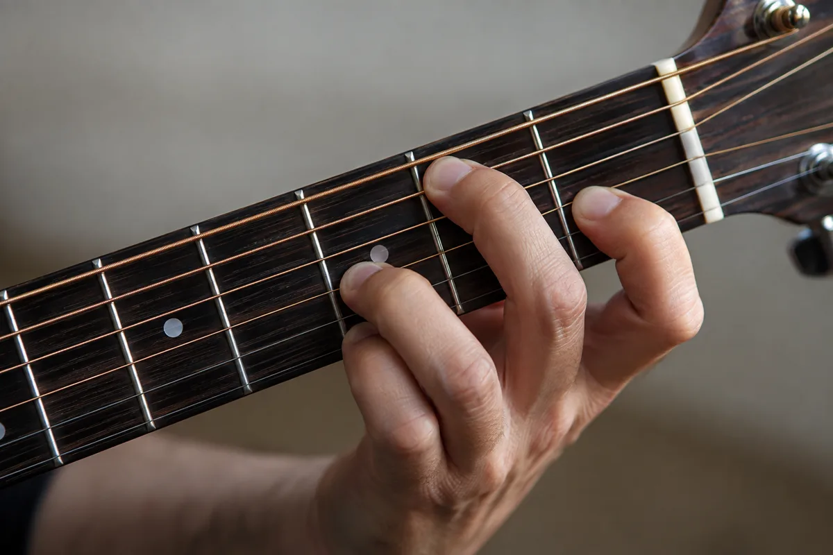 Main gauche d&rsquo;un guitariste plaquant un accord sur le manche d&rsquo;une guitare folk