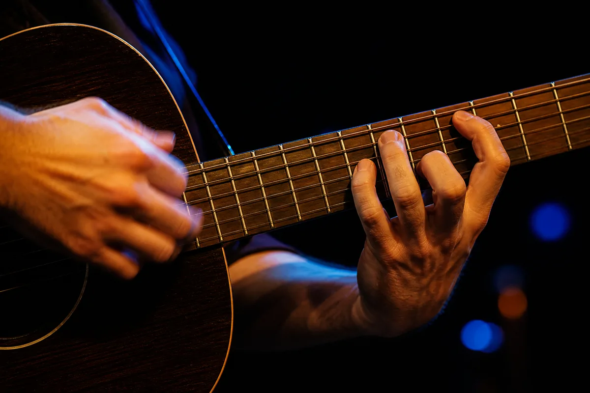 Mains d’un guitariste en gros plan sur les cordes pendant un concert
